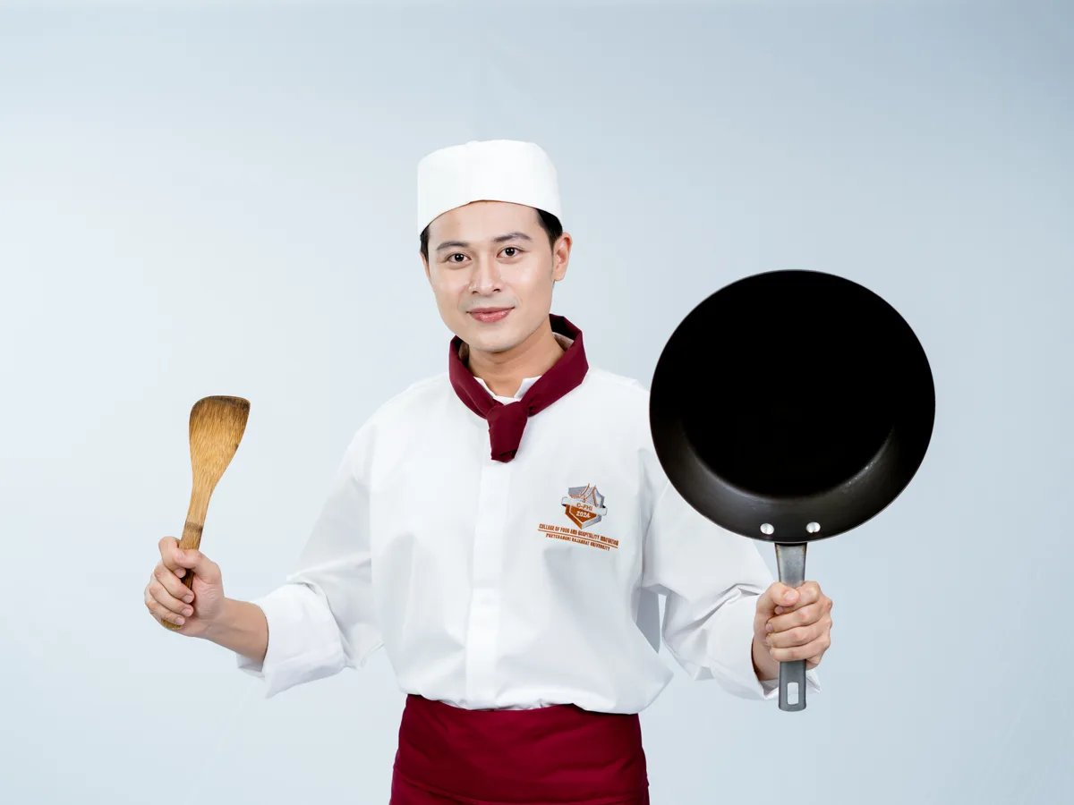 Creative gastronomy student in chef whites holding a wok and wooden spatula