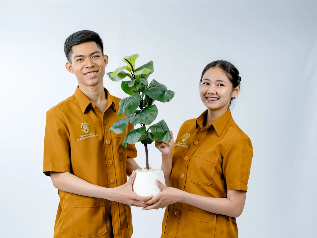 Organic agriculture students in brown shirts holding a potted plant